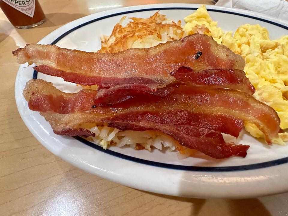 Stripes of bacon on plate of hash browns and eggs at ihop