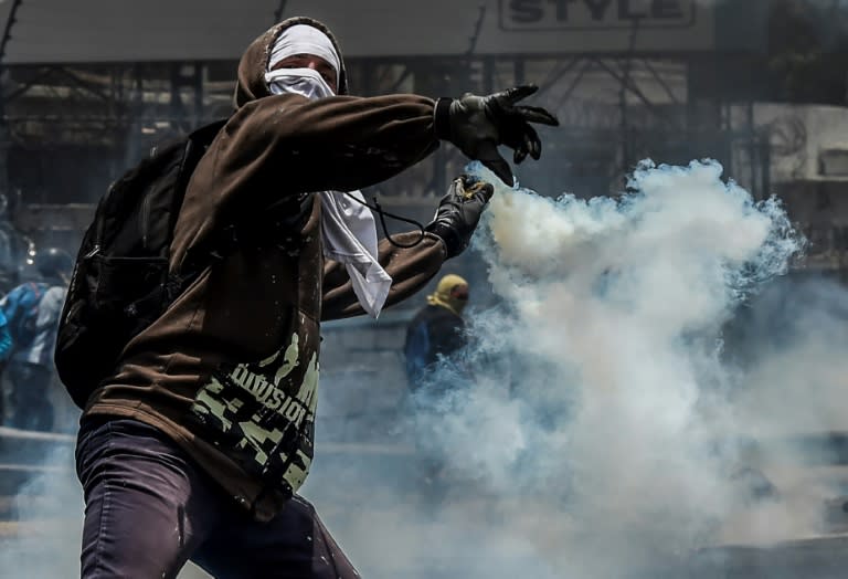 A demonstrator protesting against President Nicolas Maduro's government throws back a tear gas grenade at riot police in Caracas on April 10, 2017