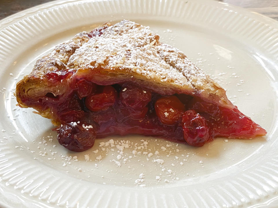 An image of a slice of cherry pie on a white plate, with icing sugar dusted on top of the pie's crust