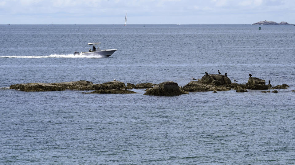 A boat glides past a rocky outcrop off Mingo Beach, in Beverly, Mass., Wednesday, June 15, 2022. The beach was named after enslaved African American Robin Mingo, who according to legend, was promised his freedom if the tide ever receded enough for him to walk out onto a rocky ledge offshore that becomes exposed at low tide. Students and faculty at Endicott College in Beverly are researching the local legend and proposing ways to memorialize Mingo. (AP Photo/Steven Senne)