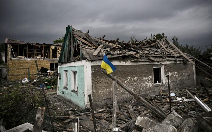 A Ukrainian flag is placed in front of a destroyed house after a strike in the city of Dobropillia - ARIS MESSINIS / AFP