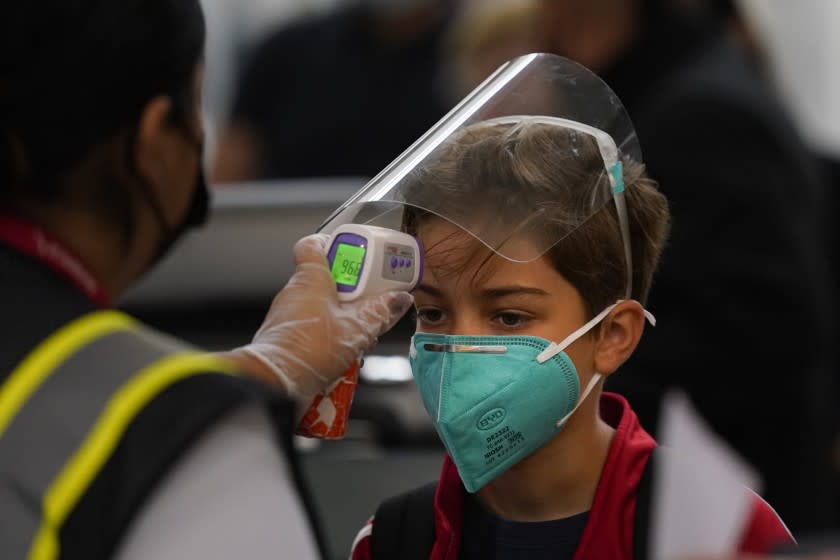 A boy gets his temperature checked while waiting in line to check in at the Los Angeles International Airport in Los Angeles, Monday, Nov. 23, 2020. About 1 million Americans a day packed airports and planes over the weekend even as coronavirus deaths surged across the U.S. and public health experts begged people to stay home and avoid big Thanksgiving gatherings. (AP Photo/Jae C. Hong)