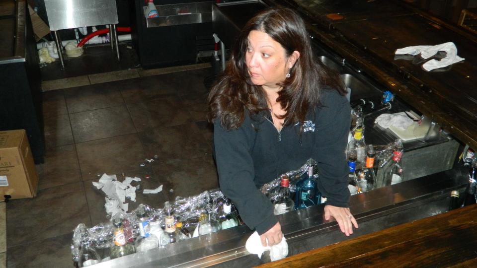 In this March 31, 2014 photo, Gigi Liaguno-Dorr cleans the bar at Jakeabob's, the Union Beach N.J. restaurant she used to operate until having to close it the previous weekend. Trash from a fundraiser the night before is on the bar's floor. The original Jakeabob's was destroyed in Superstorm Sandy, and she moved the business a few blocks inland for 2013. But a continuing inability to get timely rebuilding aid forced her to close the restaurant for good on March 28. The reopening of Jakeabob 's was seen as an inspiration to the still-struggling Raritan Bay community. (AP Photo/Wayne Parry)