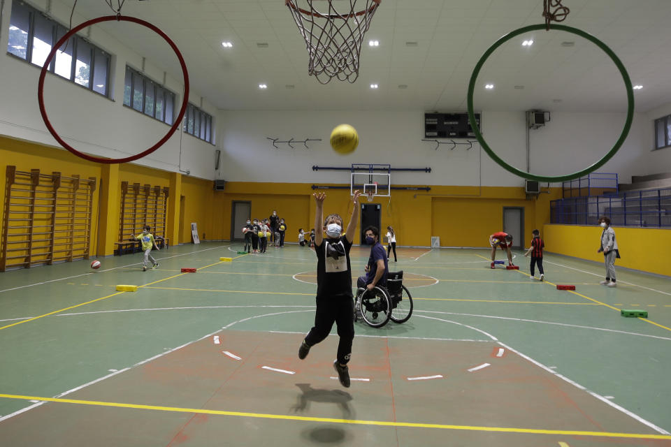 Adolfo Damian Berdun, of Argentina, a professional player and captain of the Argentine basketball Paralympic team, teaches children basketball at a primary school in Verano Brianza, outskirt of Milan, Italy, Tuesday, May 11, 2021. Four second-grade classes in the Milan suburb of Verano Brianza have been learning to play basketball this spring from a real pro. They also getting a lesson in diversity. Their basketball coach for the last month has been Adolfo Damian Berdun, an Argentinian-Italian wheelchair basketball champion. Berdun, 39, lost his left leg in a traffic accident at ag 13 in his native Buenos Aires, and he has visited many schools over the years to discuss how he has lived with his disability. (AP Photo/Luca Bruno)