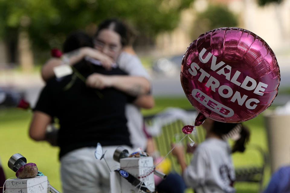 Visitors hug as they place flowers at a memorial in Uvalde, Texas, Wednesday, May 24, 2023. One year ago a gunman killed 19 children and two teachers inside a fourth-grade classroom at Robb Elementary School in Uvalde. (AP Photo/Eric Gay)