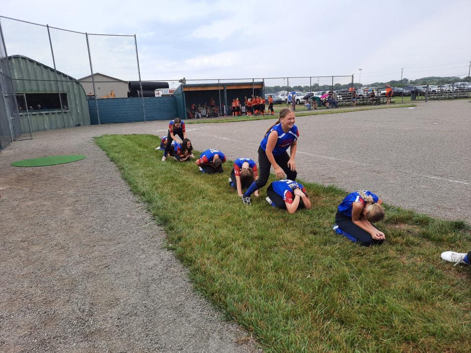 Members of Monroe's Monroe County Fair Softball Team play leapfrog as they wait out a delay Tuesday.