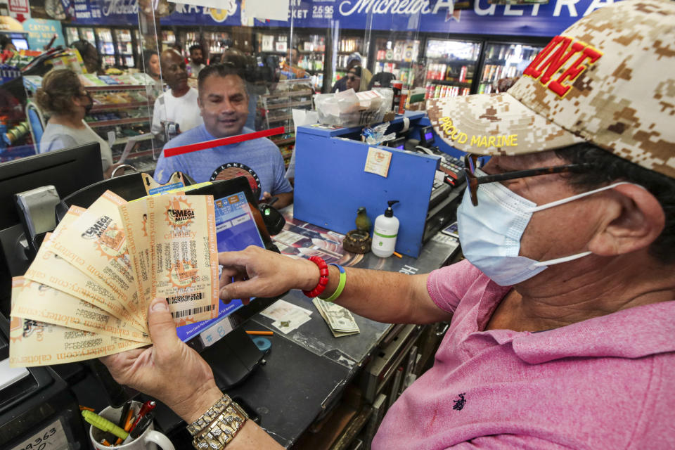 Hawthorne, CA - July 29: Ronald Marine, right, sells $200 worth of Mega Millions lottery to Paul Sandoval, as jackpot tops $1 billion at Bluebird Liquor on Friday, July 29, 2022 in Hawthorne, CA. (Irfan Khan / Los Angeles Times via Getty Images)