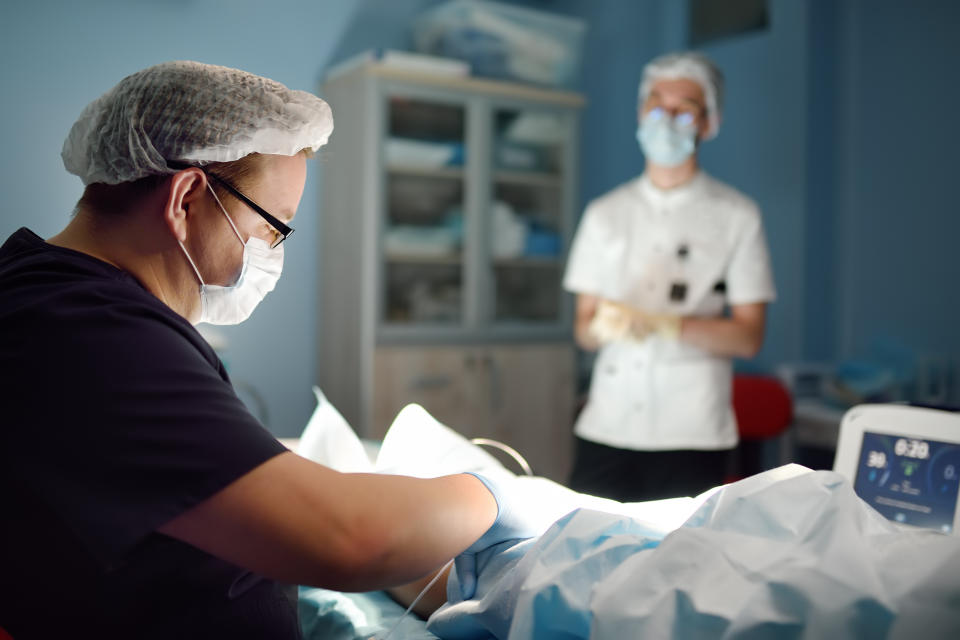 Professional vascular surgeon and assistant in the operating room of the clinic during vein surgery. Phlebectomy. A team of professional doctors during their work in the operating room.