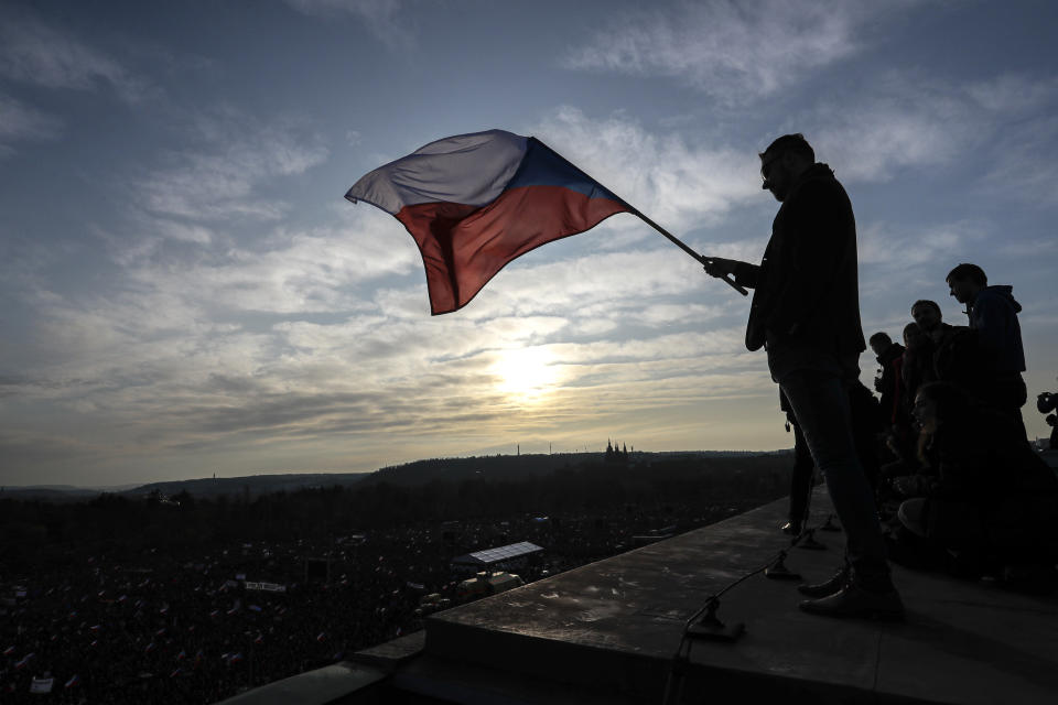A man waves a Czech flag from a roof as people take part in a large anti-government protest in Prague, Czech Republic, Saturday, Nov. 16, 2019. Czechs are rallying in big numbers to use the 30th anniversary of the pro-democratic Velvet Revolution and urge Prime Minister Andrej Babis to resign as peaceful protesters from all corners of the Czech Republic are attending the second massive protest opposing Babis at Letna park, a site of massive gatherings that significantly contributed to the fall of communism in 1989. (AP Photo/Petr David Josek)