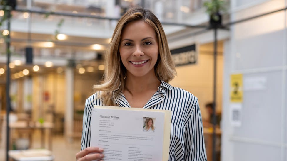 Mujer sosteniendo su CV frente a la cámara.