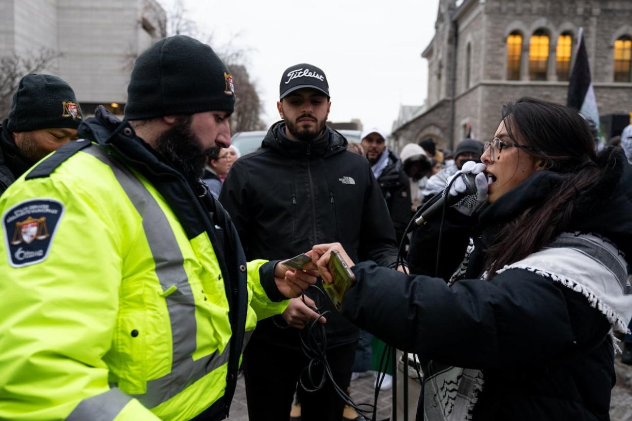 A pro-Palestinian protester, right, chants as they receive an Ottawa bylaw ticket during a demonstration on Dec. 23, 2023. The city's bylaw services now says they handed out another nine fines at a separate protest just before the New Year. (Spencer Colby/The Canadian Press - image credit)