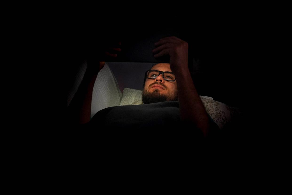 A man in a dimly lit room holding up an ipad.