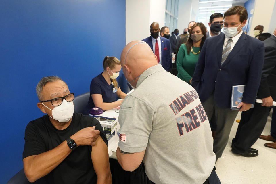 FILE - In this Jan. 4, 2021, file photo, Florida Gov. Ron DeSantis, right rear, watches as Carlos Dennis, left, 65, rolls up his sleeve so that Miami-Dade County Fire Rescue paramedic, Capt. Javier Crespo, can administer a COVID-19 vaccine shot at Jackson Memorial Hospital in Miami. With frustration rising over the slow rollout of the vaccine, state leaders and other politicians are turning up the pressure, improvising and seeking to bend the rules to get shots in arms more quickly. (AP Photo/Wilfredo Lee, File)