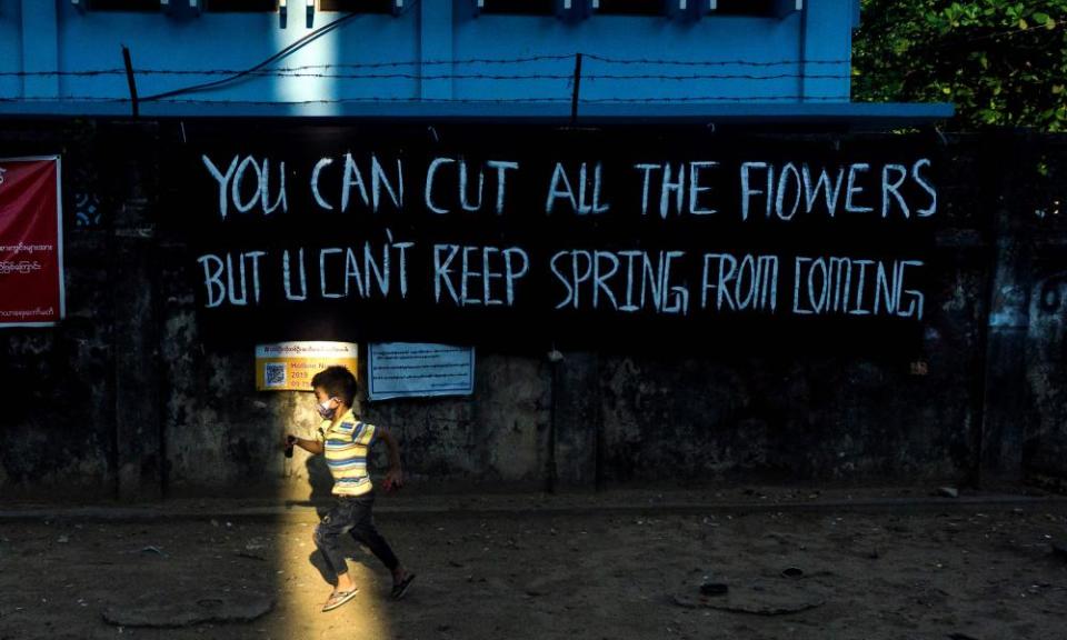 Children play with toy guns next to a banner put up by activists in protest against the military coup in Yangon