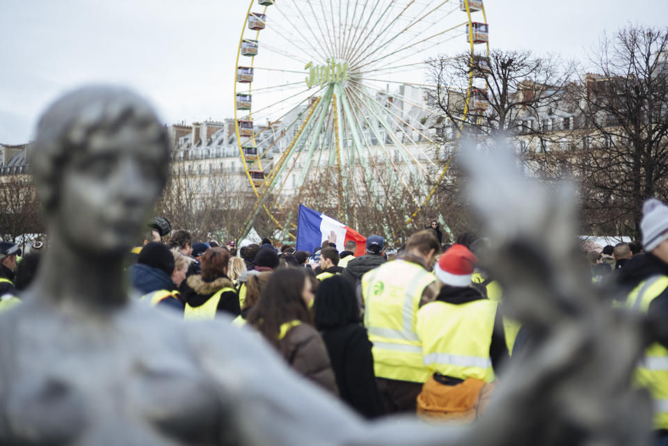 A French flag is waved by demonstrators wearing yellow vests walking in the Tuileries Garden in Paris Saturday, Dec. 22, 2018. A few hundred protesters cordoned by police forces did walk across Paris toward the Madeleine Church near the Elysee Palace but were stopped by police in a small adjacent street as some shop owners closed down early. Tempers frayed and police fired tear gas to repel protesters trying to break through the officers' line. (AP Photo/Kamil Zihnioglu)