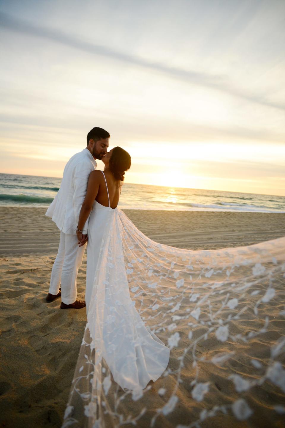 A bride and groom kiss on a beach.