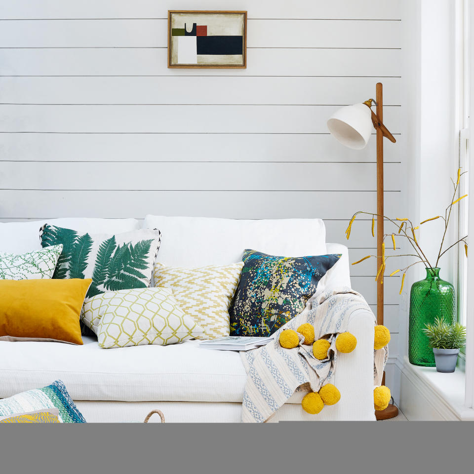 White linen sofa  with yellow and green cushions in front of white panelled wall