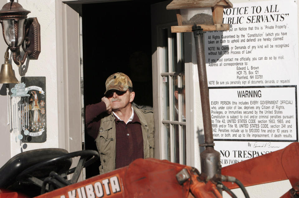 FILE - In this Jan. 17, 2007 file photo, Edward Brown stands barricaded in the doorway of his home in Plainfield, N.H., saying he is prepared for an armed standoff. Brown is up for re-sentencing Tuesday Sept. 29, 2020 over a months long armed standoff with U.S. marshals in 2007 to protest a tax evasion conviction. Brown, originally sentenced to 37 years in prison, says he should be sentenced to the 13 years he has already served. ( (AP Photo/Jim Cole, File)