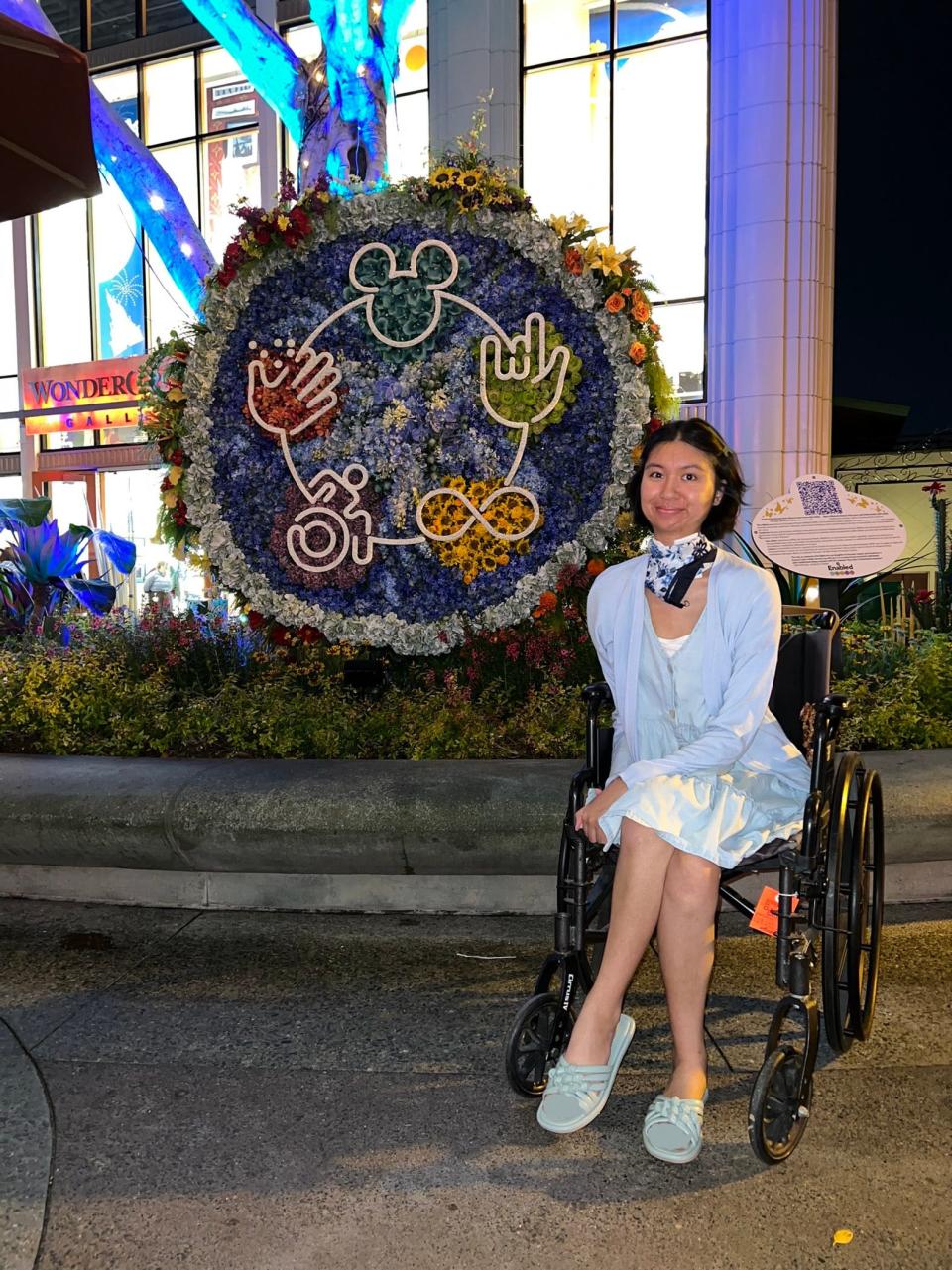 Charisma Mangahas sits beside a Disney topiary and plaque that reads "Enabled."