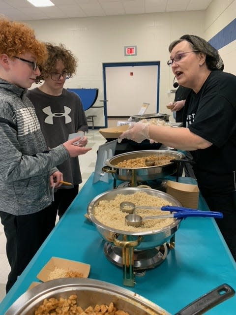 Marilyn Rosenwarne, director of dining services for Chartwells food-service company, serves Korean chicken bulgogi to Centreville eighth-grade students Mason Marchand and Jeffery Holbrook at lunchtime Wednesday.