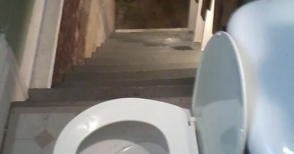 Toilet positioned at the top of a staircase, creating a dangerous and unusual setup