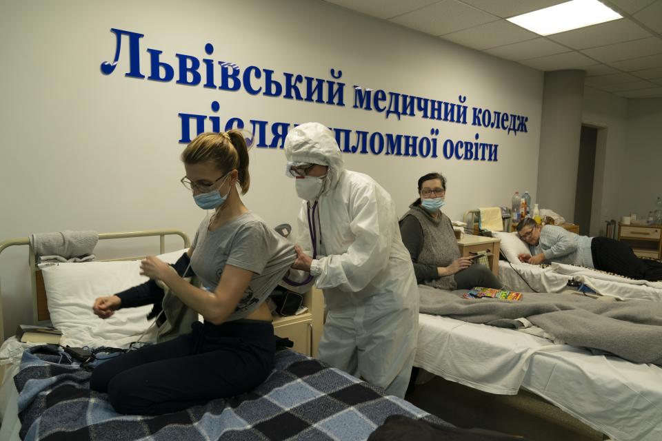 A medical worker checks on a coronavirus patient with a stethoscope in a hospital organized in the medical college in Lviv, Western Ukraine, on Monday, Jan. 4, 2021. A medical college in western Ukraine has been transformed into a temporary hospital as the coronavirus inundates the Eastern European country. The foyer of the college in the city of Lviv holds 50 beds for COVID-19 patients, and 300 more were placed in lecture halls and auditoriums to accommodate the overflow of people seeking care at a packed emergency hospital nearby. (AP Photo/Evgeniy Maloletka)