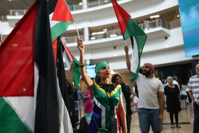 South Africans wave Palestinian flags as they wait to greet members of the country's legal team bringing a case against Israel at The Hague (Alaister Russell)