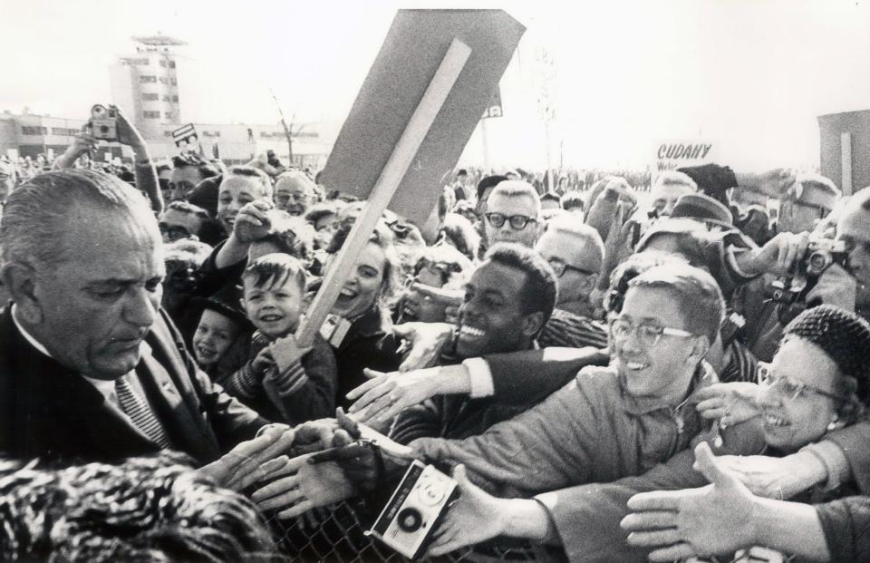 President Lyndon B. Johnson, left, grimaces after he jammed his hand against the fence holding back the crowd at the Milwaukee airport yesterday. Johnson's hands are bandaged from the continual handshaking on the campaign but he stopped his motorcade several times during the Milwaukee in1964.