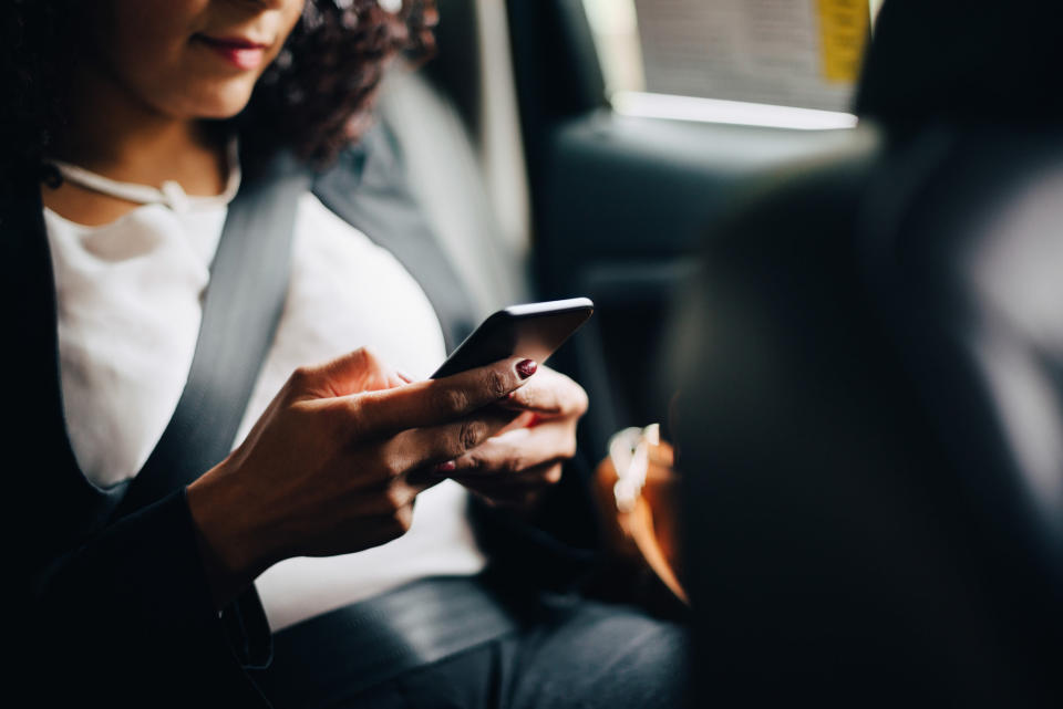 A woman sitting in a car and wearing a seatbelt while on her cellphone