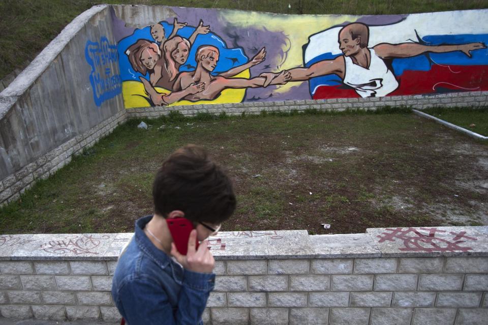 A Ukrainian woman passes by a wall covered with graffiti showing the flags of Ukraine and Russia united in Simferopol, Crimea, Tuesday, March 25, 2014. (AP Photo/Pavel Golovkin)