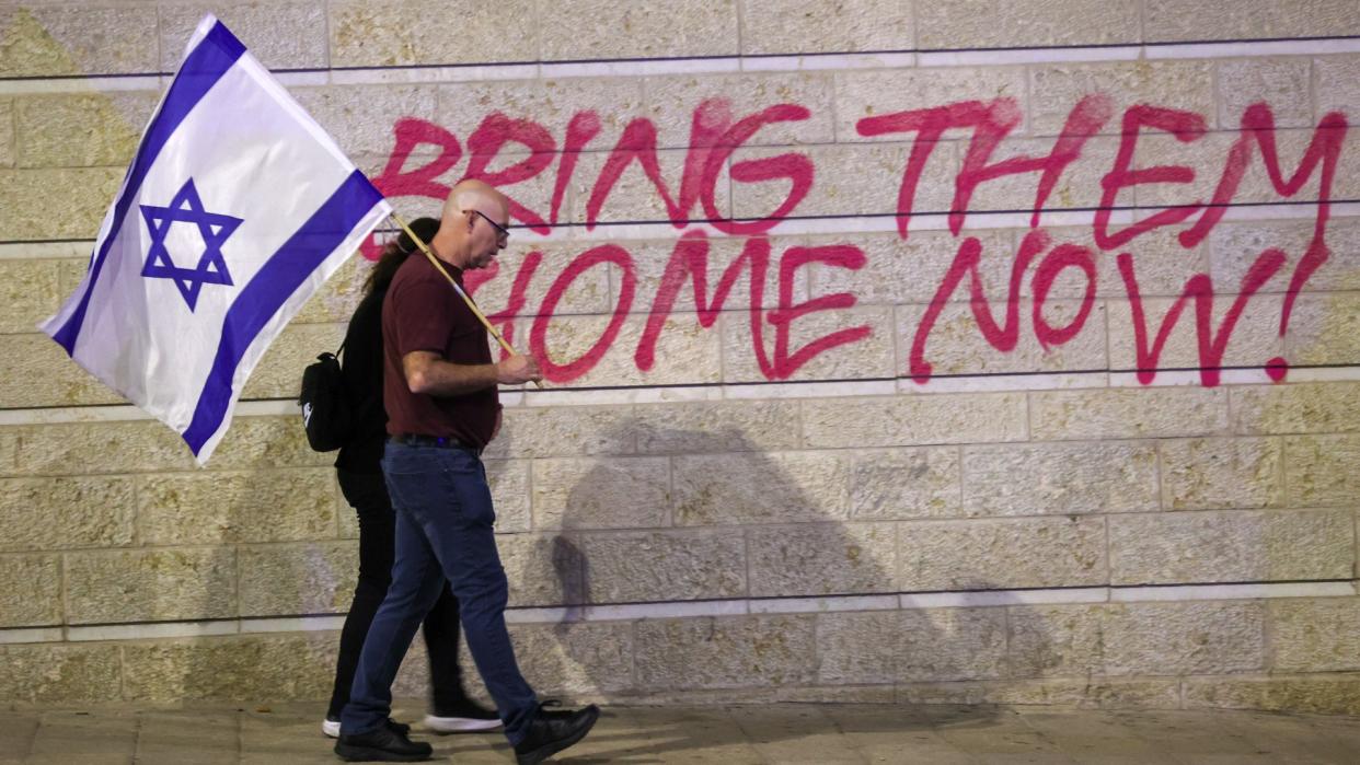  A couple holding an Israel flag walk past a protest wall. 