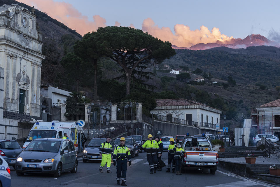 Italian Civil protection volunteers gather near the heavily damaged church of Maria Santissima as plumes of smoke come out the Mount Enta Volcano in Fleri, Sicily Italy, Wednesday, Dec. 26, 2018. A quake triggered by Italy's Mount Etna volcano has jolted eastern Sicily, slightly injuring 10 people and prompting frightened Italian villagers to flee their homes. (AP Photo/Salvatore Allegra)