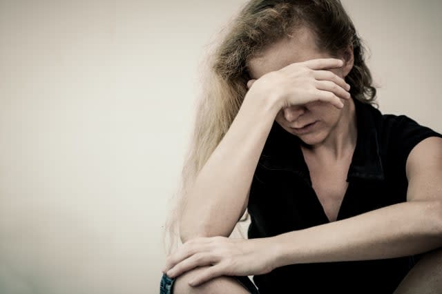 one sad woman sitting on the floor near a wall and holding her head in her hands