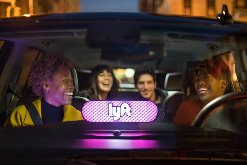 A lighted Lyft logo mounted on the dashboard of a car with driver and passengers laughing