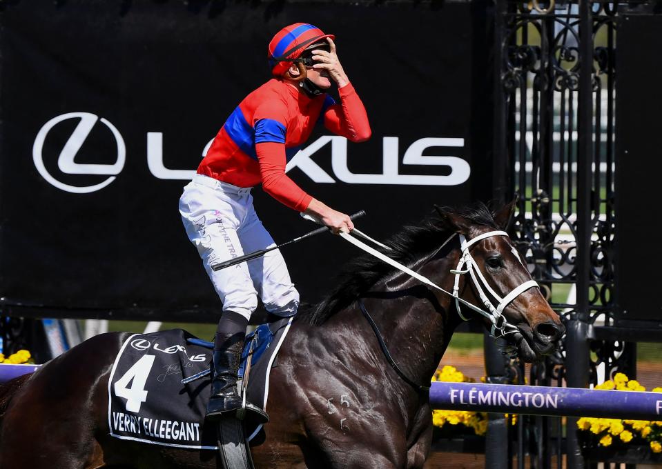 A jockey with his hand over his eyes stands in the stirrups of his horse after winning a race.