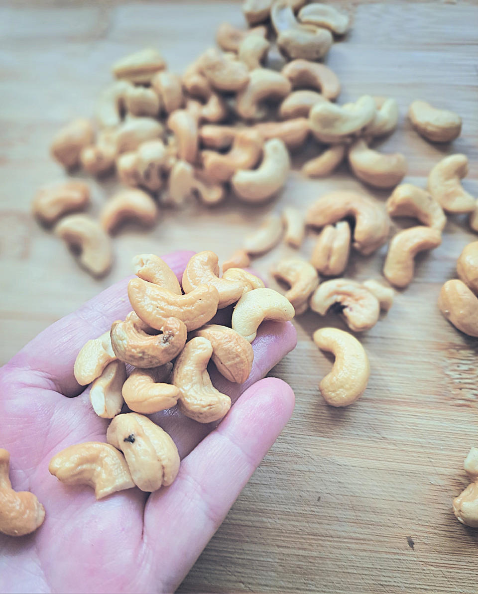 A hand holds several cashews, with more cashews scattered on a wooden surface in the background