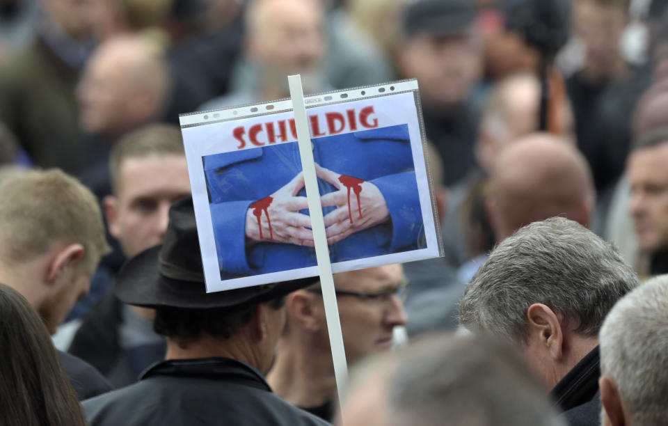 A demonstrator holds a poster with Angela Merkel's trademark gesture and the word 'guilty' during a demonstration in Chemnitz, eastern Germany, Saturday, Sept. 1, 2018, after several nationalist groups called for marches protesting the killing of a German man last week, allegedly by migrants from Syria and Iraq. (AP Photo/Jens Meyer)