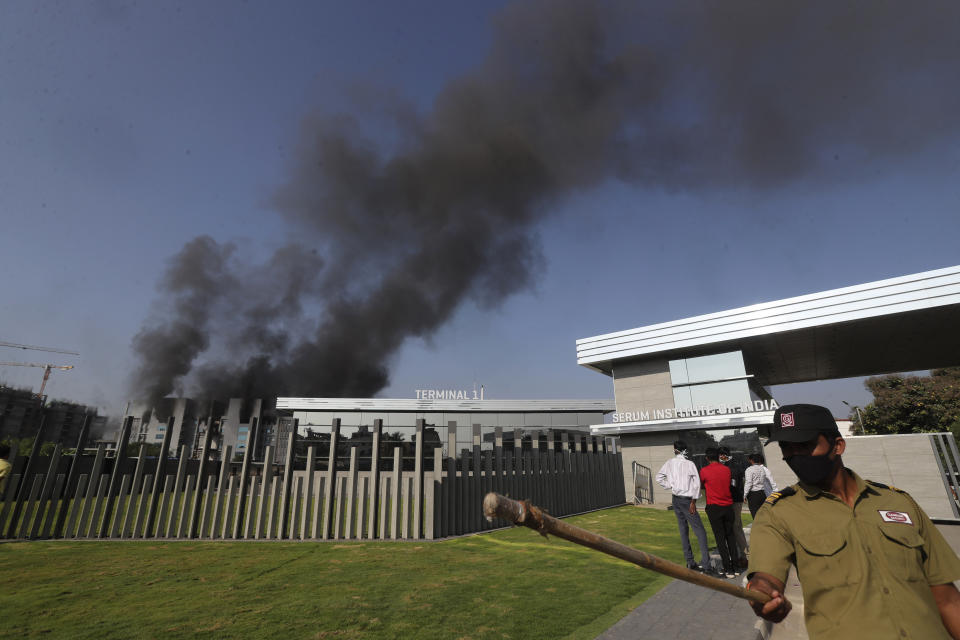 A security man tries to keep people away as smoke rises from a fire at Serum Institute of India, the world's largest vaccine maker that is manufacturing the AstraZeneca/Oxford University vaccine for the coronavirus, in Pune, India, Thursday, Jan. 21, 2021. (AP Photo/Rafiq Maqbool)