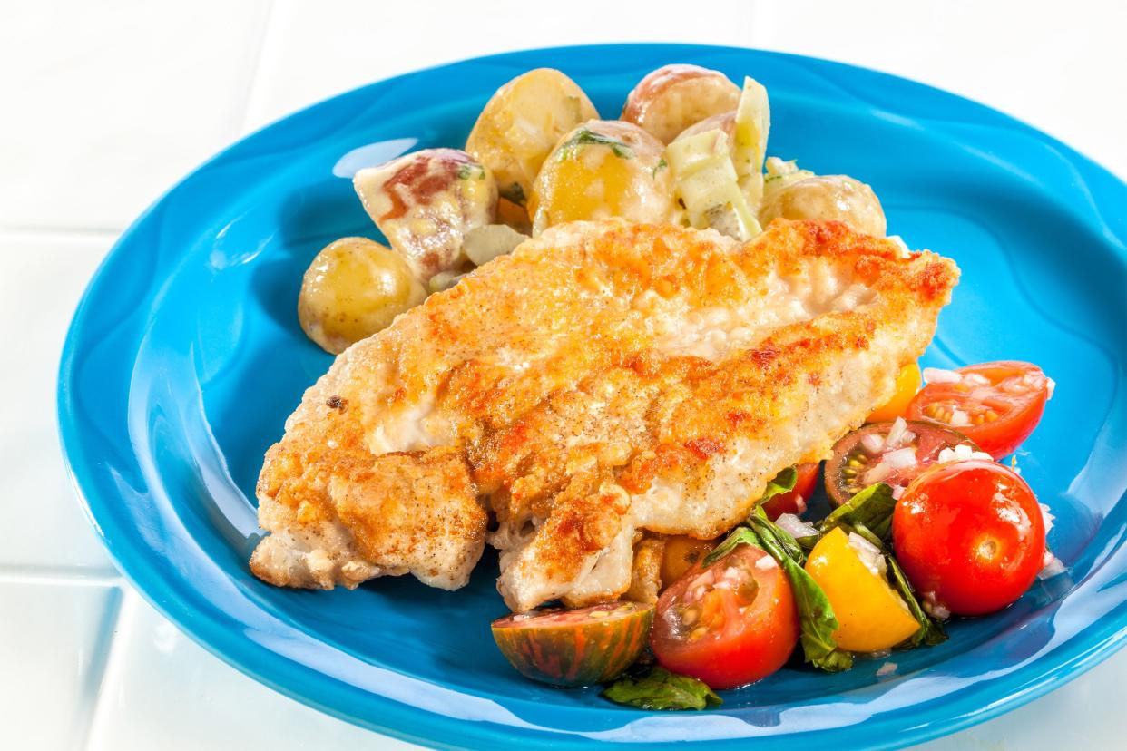 Pan-roasted chicken paillard with potato salad and tomatoes on a blue plate on a white tile table