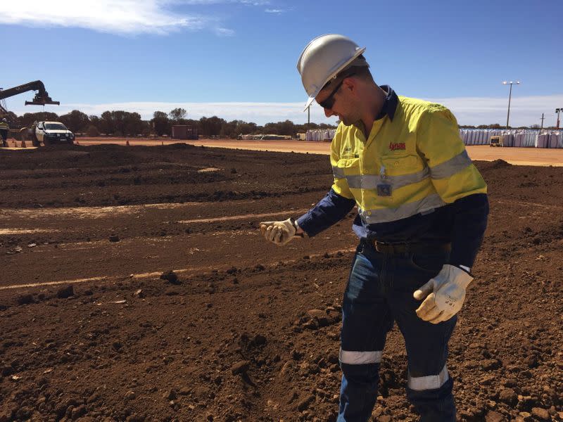 FILE PHOTO: A worker picks up a handful of rare earth concentrate that has been left to dry in the sun before it is packed and shipped to Malaysia for further processing, at Mount Weld, northeast of Perth, Australia