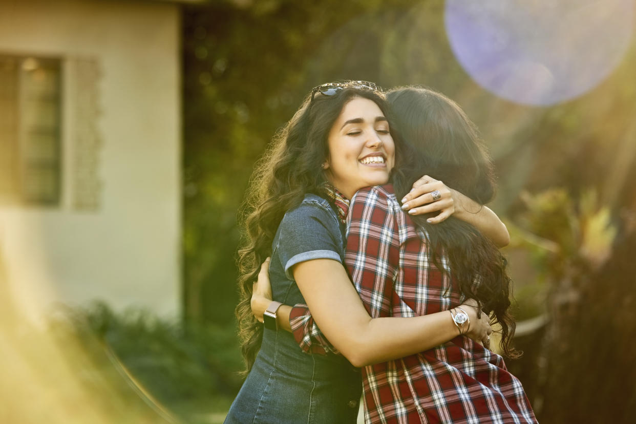 Smiling young woman welcoming friend for backyard party. Female are socializing on weekend. They are wearing casuals.