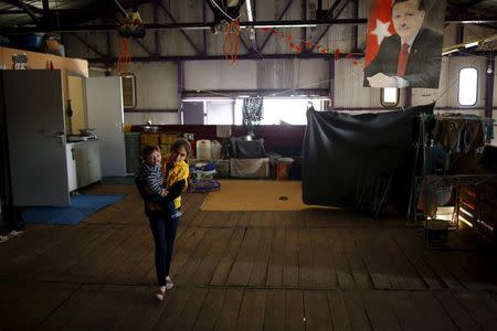 A Syrian refugee girl carries her sister in a building in Yayladagi refugee camp in Hatay province, near the Turkish-Syrian border, Turkey, December 15, 2015. A portrait of Turkey's President Tayyip Erdogan hangs from the ceiling. REUTERS/Umit Bektas