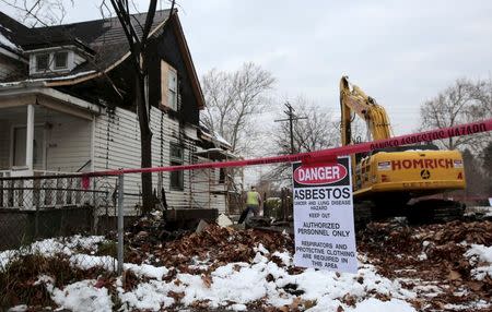 A "Danger Asbestos" sign is seen as a demolition crew removes the remains of a demolished home, next to an occupied one, in a neighborhood filled with blight in Detroit, Michigan, November 24, 2015. REUTERS/Rebecca Cook