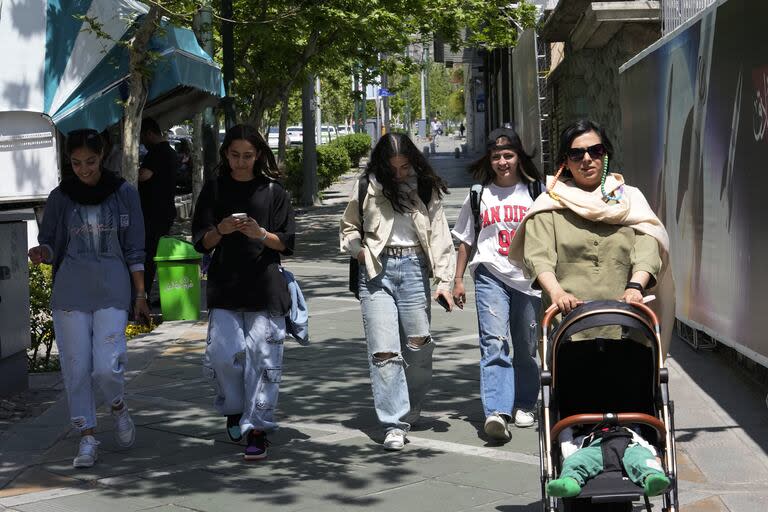 Mujeres iraníes sin usar el velo islámico obligatorio caminan por una acera en el norte de Teherán, Irán, el viernes 19 de abril de 2024. 