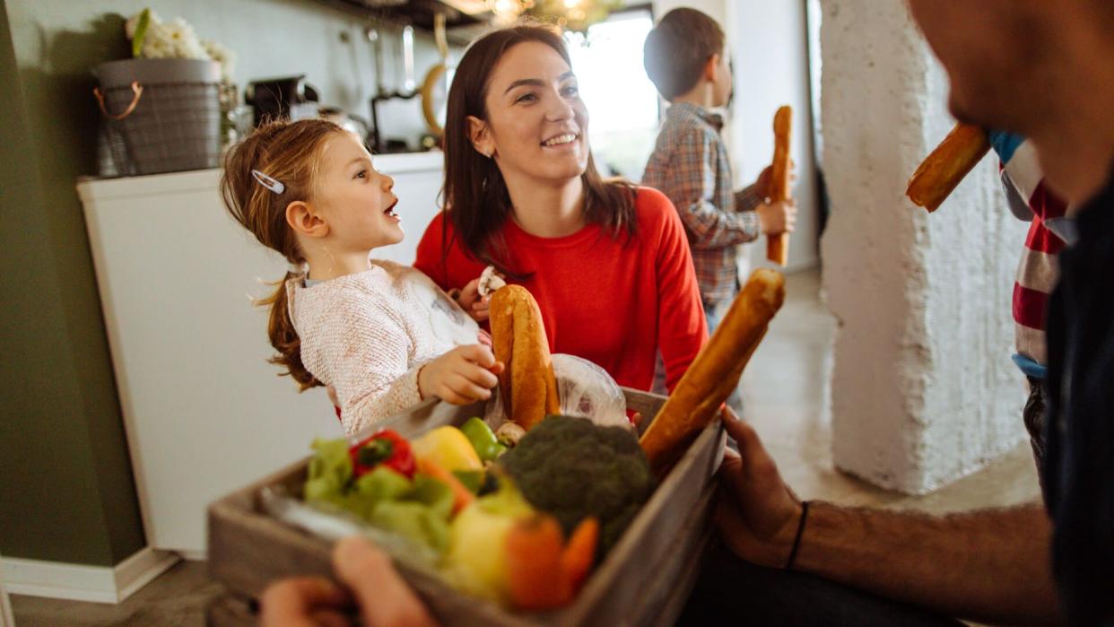 Photo of a delivery person delivering package of fresh groceries to a stay-at-home mother and her children.