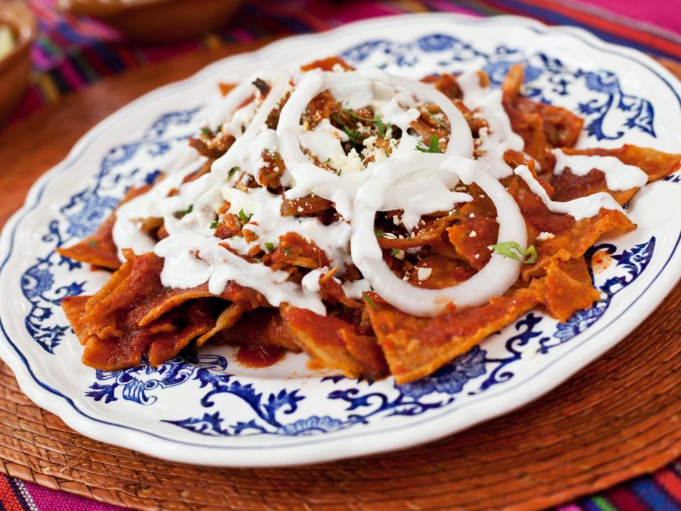 chilaquiles on a white and blue plate on a wood tray