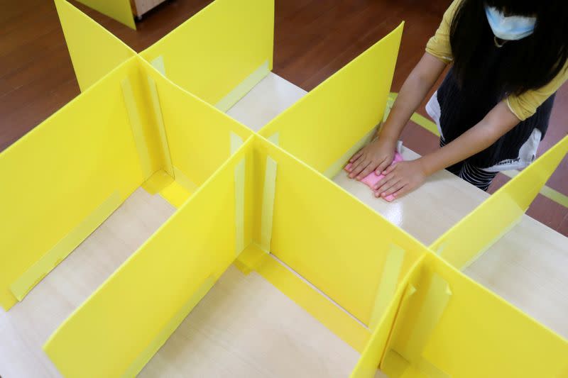 A pupil wipes a desk with yellow dividers at Dajia Elementary school in Taipei