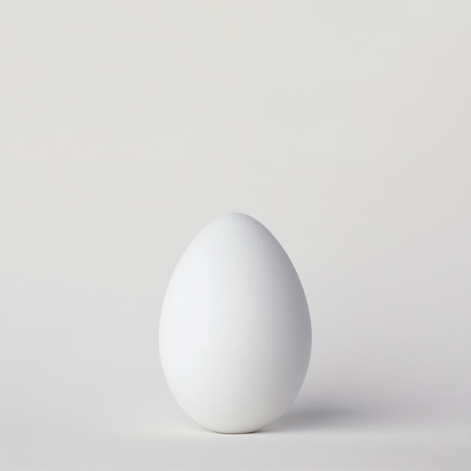 A plain, single egg standing upright on a neutral background