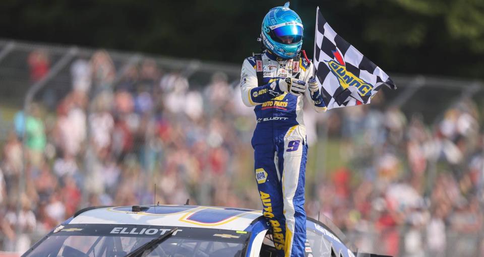 Chase Elliott stands atop his No. 9 Hendrick Motorsports Chevrolet and waves the checkered flag to the crowd following his NASCAR Cup Series victory at Road America. 