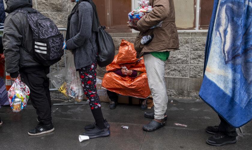 LOS ANGELES, CA - DECEMBER 25: People stand in line to receive a Christmas meal and hygiene kits from volunteers in Skidrow at The Midnight Mission on Christmas Day on Saturday, Dec. 25, 2021, in Los Angeles, CA. (Francine Orr / Los Angeles Times)